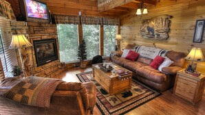 A cozy cabin interior with a stone fireplace, leather sofa, and a television mounted on the wall.