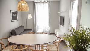 A modern living room with a round dining table, wooden chairs, a grey sofa, a floor lamp, and a TV mounted on the wall. - Flats Friends Soho Suites (Valencia)