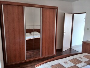 A bedroom with a wooden wardrobe, a bed with a quilt, and a door leading to another room. - Room in Apartment - Apartments and Rooms With a Swimming Pool Kampor - rab (Rab)