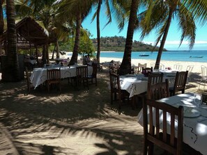 Un espace de restauration en plein air avec des tables et des chaises, des palmiers et une vue sur la plage.