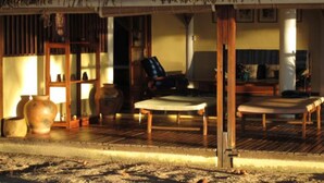 A traditional thatched-roof structure with a wooden floor, a sofa, and a chair.