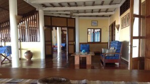 A spacious room with a wooden floor, a large woven mat, a traditional woven chair, a wooden table, and a large vase. - Nosy be, a Wonderful Location to Have a Relaxing Vacation (Nosy Be)