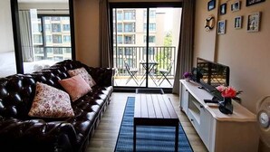 Een woonkamer met een leren bank, een kleine salontafel, een televisie en een balkon met uitzicht op gebouwen.
