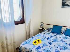 A bedroom with a bed, a nightstand, a window with curtains, and a wall-mounted lamp. - Comfy Seafront Apartment-beahost (San Michele al Tagliamento)