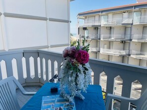 A balcony with a table set for a small event, featuring a floral arrangement and a blue tablecloth. - Comfy Seafront Apartment-beahost (San Michele al Tagliamento)