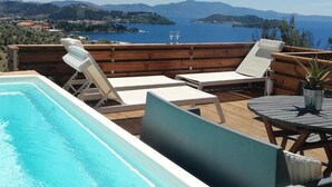 A poolside area with lounge chairs and a table, overlooking a body of water and distant hills. - 2br Suite White gea With Private Pool No01 (Skiathos)