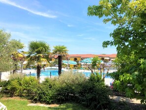 A pool area with palm trees, lounge chairs, and a building with a red roof.