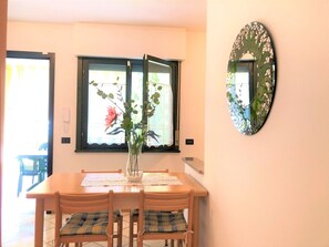 A dining area with a wooden table and chairs, a vase with flowers, a window with a view, and a decorative mirror on the wall.