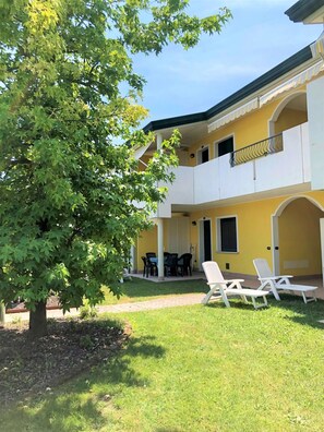 Un bâtiment à deux étages doté d’un balcon, d’un espace extérieur aménagé pour s’asseoir et d’un arbre.