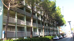A multi-story building with balconies, parked cars, and a clear sky. - Holiday in Bibione by the Beach-beahost (San Michele al Tagliamento)