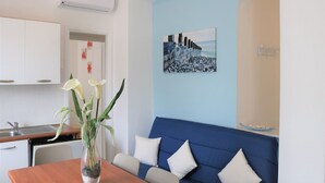 A modern living room with a blue sofa, a wooden dining table, and a vase with white flowers. - Beachfront Luminous Flat in Bibione (San Michele al Tagliamento)