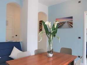 Un coin repas avec une table en bois, un vase rempli de fleurs et un tableau accroché au mur.