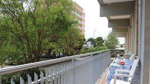 A balcony with a table and chairs, a white fence, and trees in the background. - Beachfront Luminous Flat in Bibione (San Michele al Tagliamento)