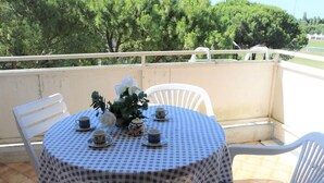 Ein Balkon mit kariertem Tisch, weißen Stühlen und einem kleinen Tisch, gedeckt mit Tassen und einer Blumenkomposition.