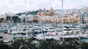 Un port de plaisance rempli de bateaux, une église imposante avec deux tours et, au loin, une colline parsemée de bâtiments.