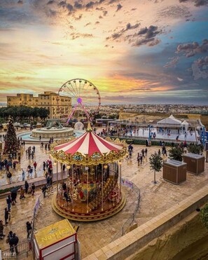 Un manège installé sur une place publique, avec une grande roue en arrière-plan.