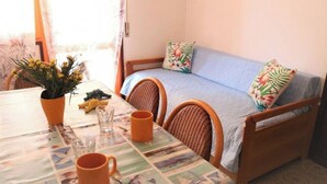 A room with a bed, two wicker chairs, a table with a floral tablecloth, and a vase with flowers. - Flat Just 80m From the Beach (San Michele al Tagliamento)