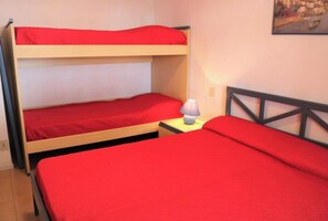 Une chambre avec un lit superposé, une literie rouge et une lampe sur une table de chevet.