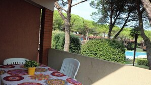Une terrasse extérieure avec une table recouverte d’une nappe colorée, un pot jaune contenant une plante et des chaises blanches.
