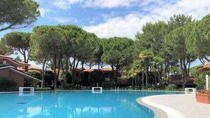 Une piscine à bords incurvés, entourée d’arbres et de bâtiments aux toits recouverts de tuiles rouges.