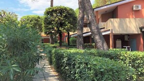 Un chemin bordé de verdure et d’arbres, qui mène à un bâtiment doté de nombreux balcons et d’une façade rouge.