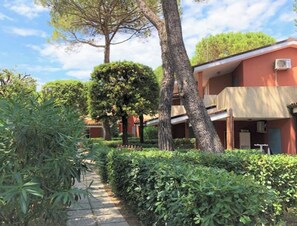 A pathway lined with greenery and trees, leading to a building with multiple balconies and a red facade.