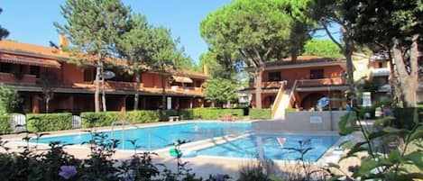 A swimming pool surrounded by lush greenery and a building with a red-tiled roof.