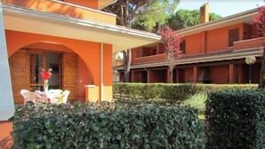 A building with an orange facade, a covered patio area with a table and chairs, and a well-maintained hedge. - Flat in a Poolside Residence-beahost (San Michele al Tagliamento)