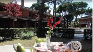 An outdoor patio with a round table, chairs, and a vase with flowers. - Flat in a Poolside Residence-beahost (San Michele al Tagliamento)
