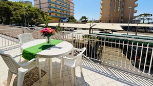A terrace with a table and chairs, a vase of flowers, and a view of a hotel building in the background. - Flat With Large Balcony in Bibione (San Michele al Tagliamento)
