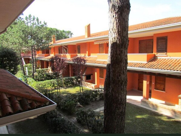 Une cour bordée de bâtiments aux façades orange, avec un arbre et un toit recouvert de tuiles.