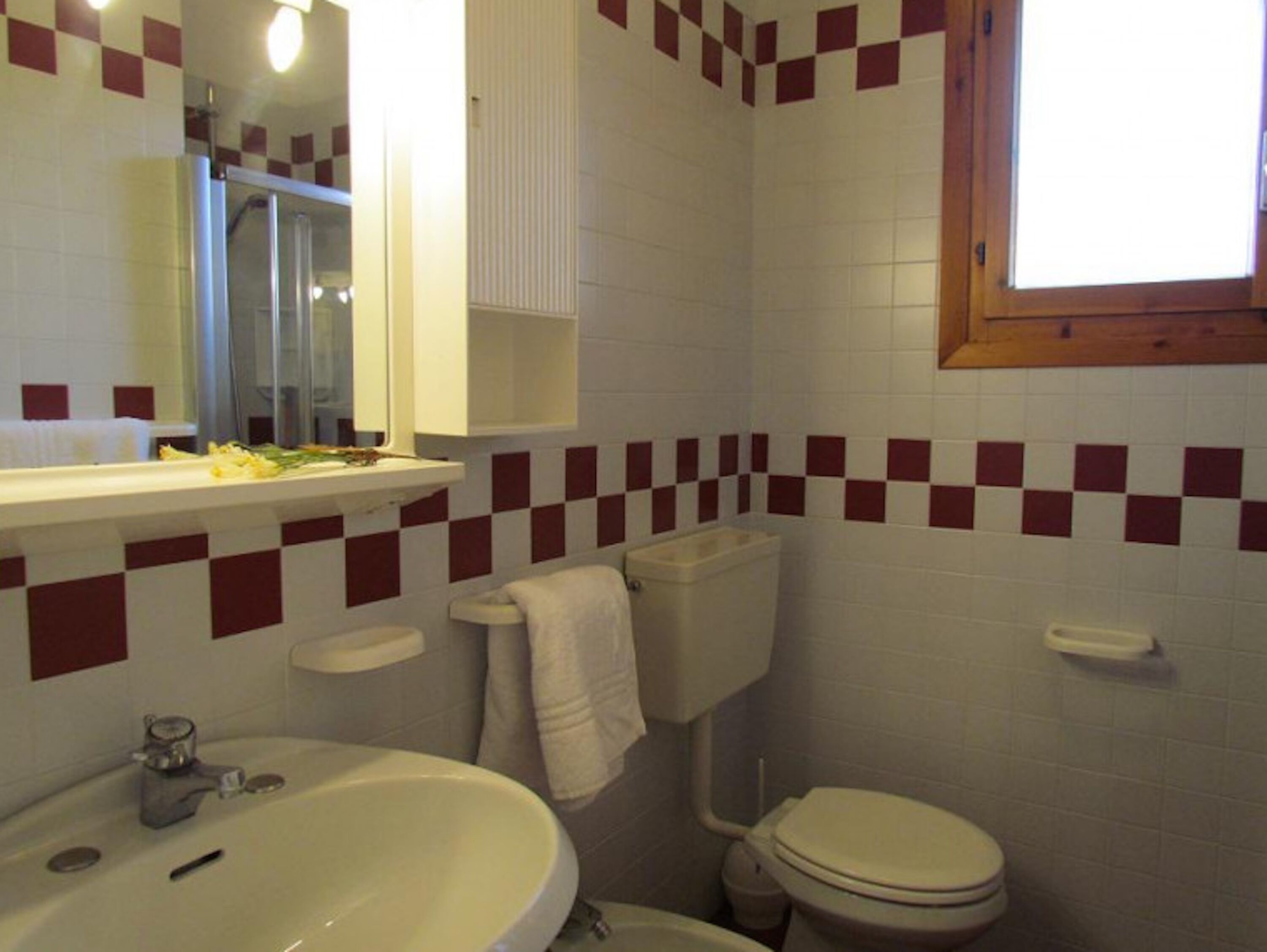 A bathroom with a sink, toilet, and mirror. The walls have a checkered tile pattern.