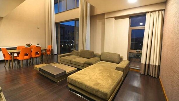 Una sala de estar moderna con un sofá modular, una mesa de comedor con sillas y ventanas grandes con vistas a la ciudad de noche.