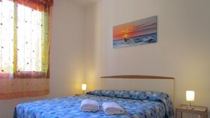 A bedroom with a bed, two bedside lamps, a painting of a sunset, and a window with curtains. - Lovely Flat With Garden and Shared Pool (San Michele al Tagliamento)