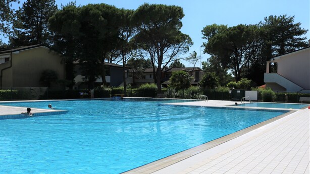A rectangular swimming pool with tiled edges, surrounded by a tiled deck. - Lovely Flat With Garden and Shared Pool (San Michele al Tagliamento)