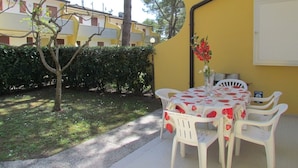 A patio with a table and chairs, a small tree, and a hedge. - Lovely Flat With Garden and Shared Pool (San Michele al Tagliamento)