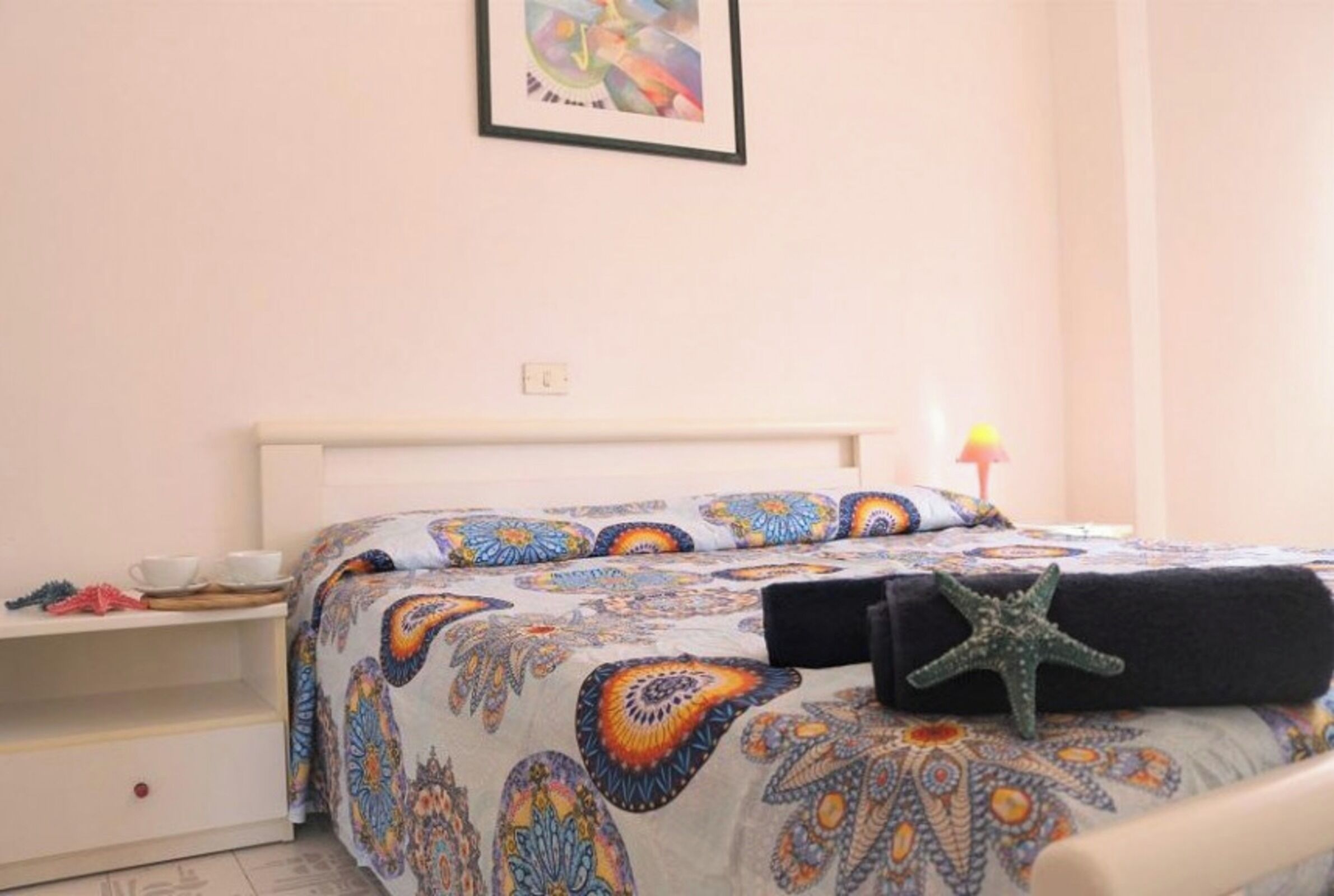 A bedroom with a bed, a nightstand, a framed picture on the wall, and a starfish decoration.