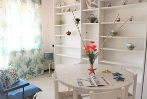 A room with a round table, a chair, a television, and shelves with various items.
