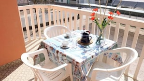 A table set with a tablecloth, a pitcher, cups, and a vase with flowers on a balcony. - Cosy Flat 80mt From the sea (San Michele al Tagliamento)