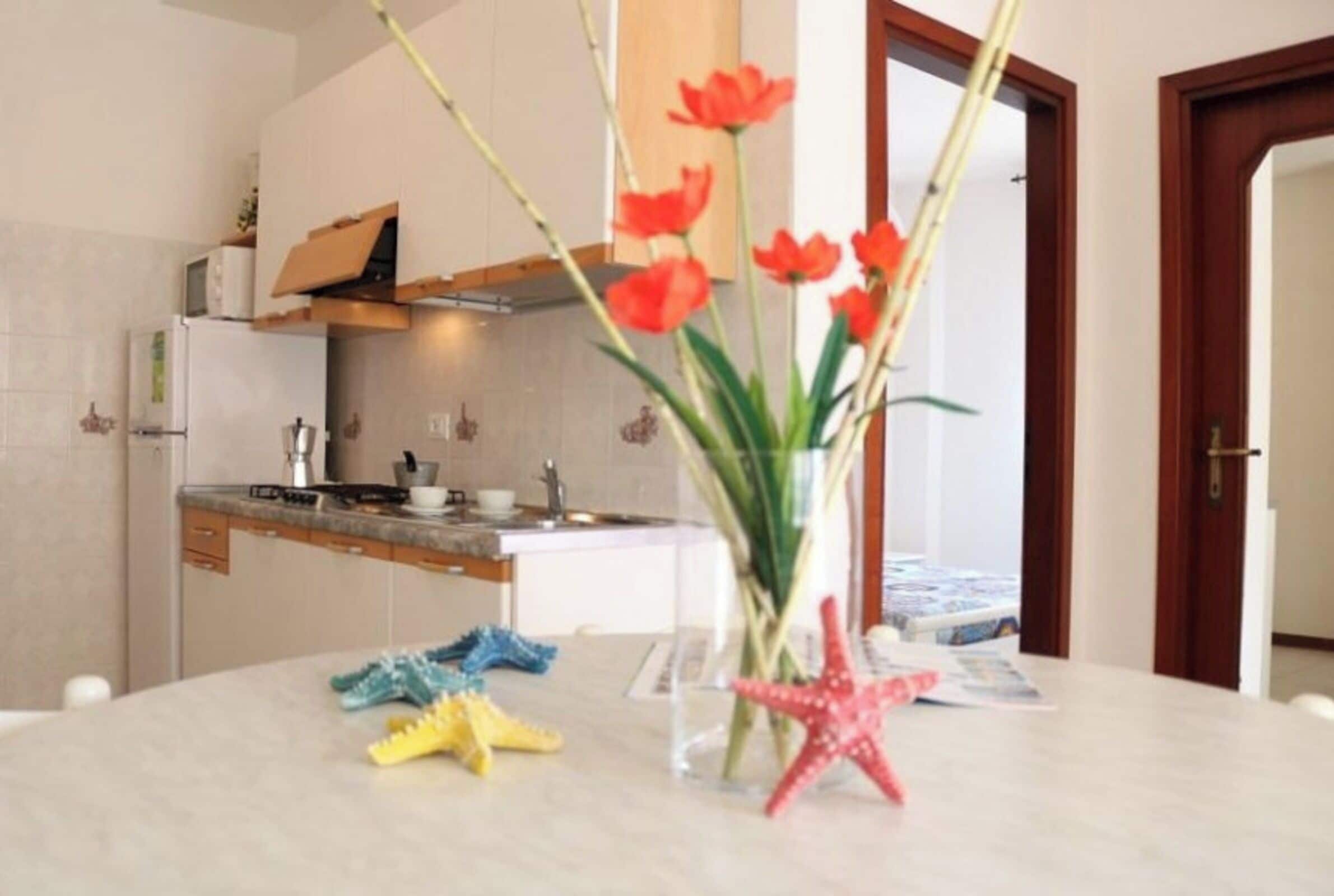 A modern kitchen with white cabinets, a built-in oven, and a countertop with a vase of flowers and starfish decorations.