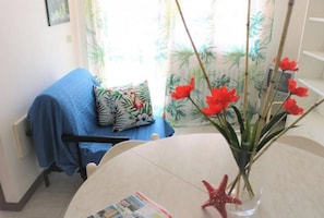 A room with a bed covered in blue, a table with a vase of red flowers, and a chair.
