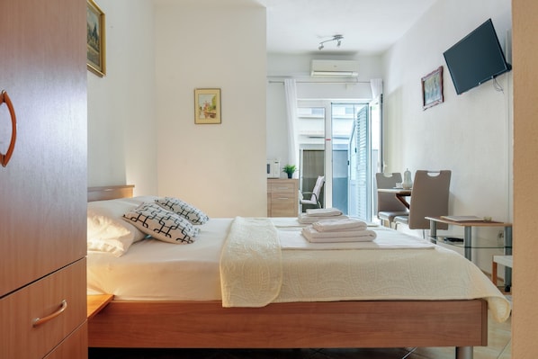 A hotel room with a bed, a desk, a chair, a TV, and a bathroom visible through an open door.