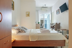 Ett hotellrum med en säng, ett skrivbord, en stol, en tv och ett badrum som syns genom en öppen dörr.
