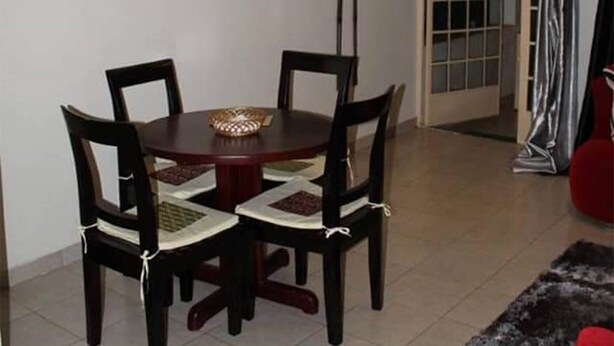 Zona pranzo con tavolo rotondo e sedie, una lampada a parete e una porta che dà su un'altra stanza.