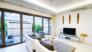 A modern living room with a sofa, a TV, and a glass coffee table. - Beautiful 1br Plunge Pool Villa Walk To Bangtao Beach (Choeng Thale)