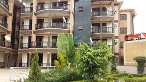 A multi-story residential building with balconies, satellite dishes, and a well-maintained garden with hedges and a central tree. - Have a Nice Stay in Your Apartment in Kampala (Kampala)