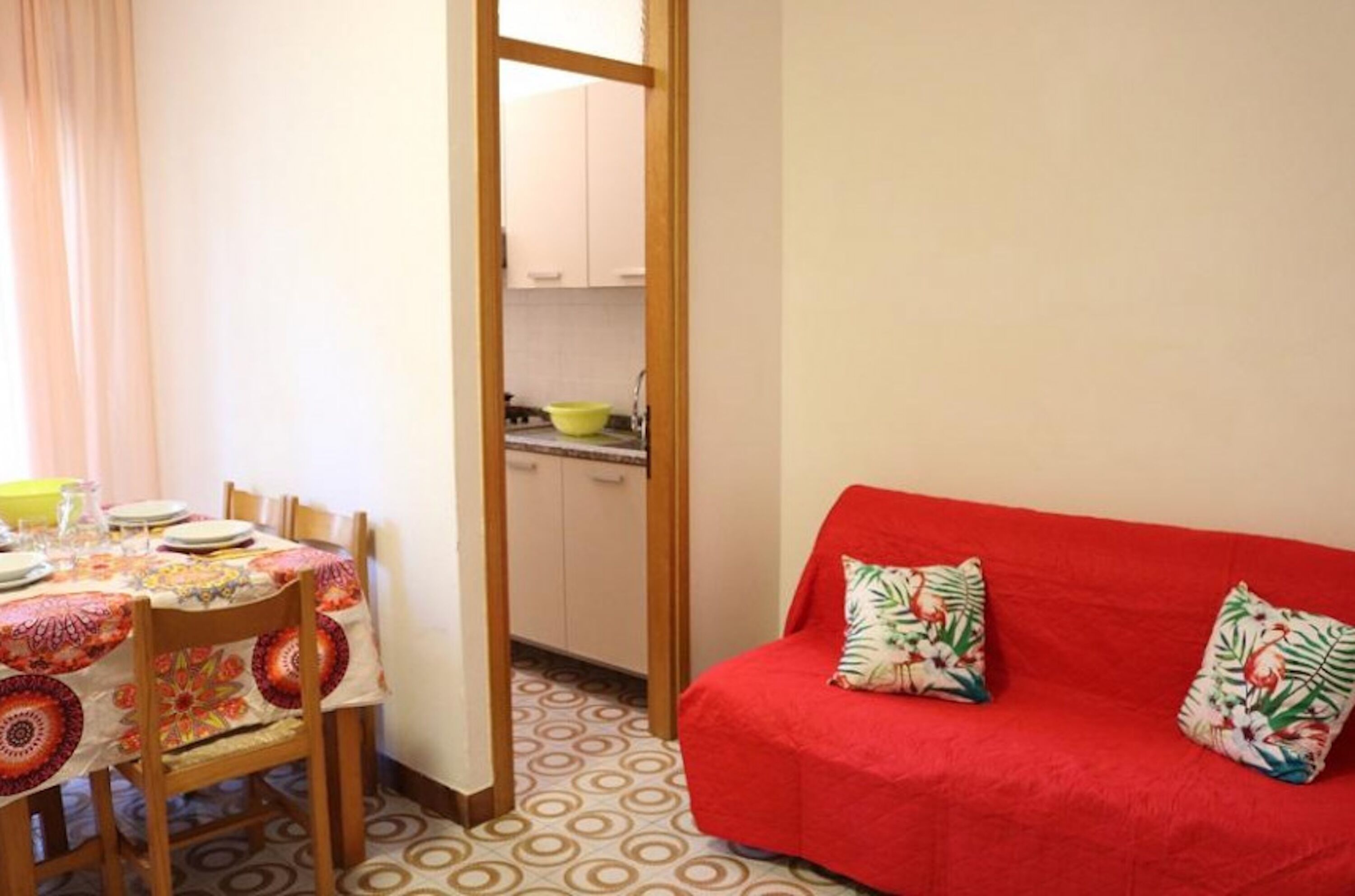 Un espace de vie compact comprenant un coin repas, une kitchenette et un canapé rouge agrémenté de coussins à motifs floraux.