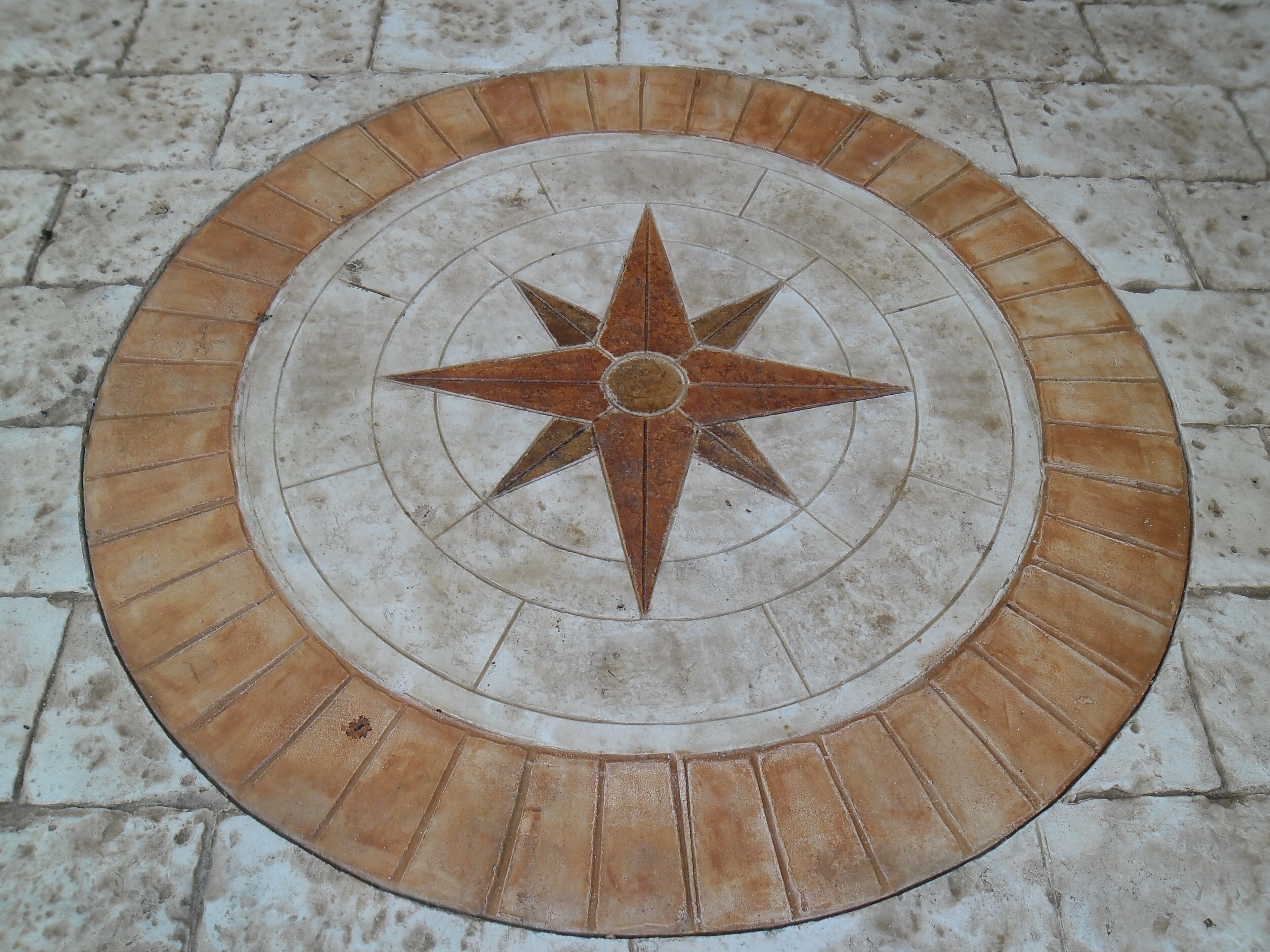 Diseño de piso circular con un motivo de estrella central rodeado de círculos concéntricos y un borde de baldosas rectangulares.