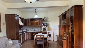 A compact kitchen with wooden cabinets, a dining table, a washing machine, and a sofa.