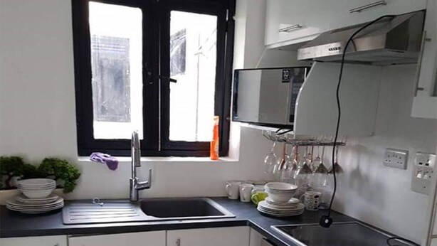 A compact kitchen with white cabinets, a black countertop, a built-in oven, and a window with a black frame. - A Cosy Fully Furnished Apartment in Kampala (Kampala)